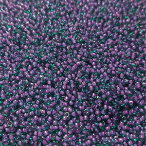 May include: A close-up view of a large quantity of small, round, purple and teal glass beads. The beads have a shiny, iridescent finish.