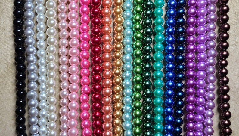 May include: Rows of colorful beads in various shades, including black, white, pink, red, orange, green, blue, purple, and brown. The beads are round and appear to be strung together, creating a vibrant display of colors.