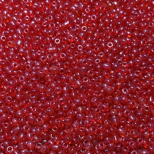 May include: A close-up image of a large quantity of small, red, round glass beads. The beads are translucent and have a slight shine.