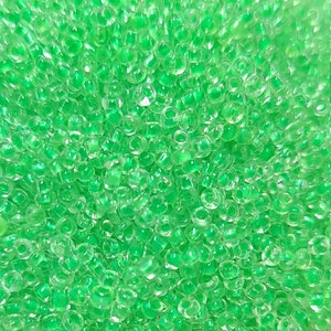May include: Close-up of a pile of small, transparent, light green glass beads. The beads are round and reflect light, creating a sparkling effect. Ideal for jewelry making and craft projects.