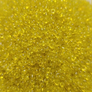 May include: A close-up image of a pile of small, round, yellow glass beads. The beads are translucent and have a slight shimmer to them.