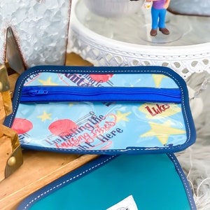 Könnte beinhalten: Eine blaue und weiße Reißverschlusstasche mit einer durchsichtigen Vinyl-Vorderseite. Die Tasche hat ein Sternenmuster und den Text "I'm feeling the knitting vibes right here" und "Lukes".