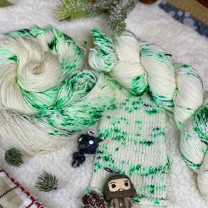 以下が含まれることがあります： 黒の斑点のある白と緑の糸、編まれたスカーフ、小さな黒い置物、ひげを生やした男性の小さな置物、そして格子縞の毛布。