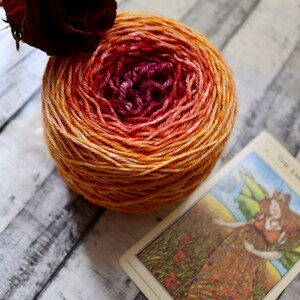 Peut inclure: Une pelote de laine avec un d&eacute;grad&eacute; de couleurs orange, jaune et rouge. Une rose s&eacute;ch&eacute;e est en arri&egrave;re-plan. Le texte "THE EMPRESS" est visible sur une carte au premier plan.