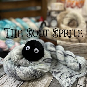May include: A skein of light blue and black yarn with a black soot sprite plush toy nestled in the center. The yarn is called "The Soot Sprite".