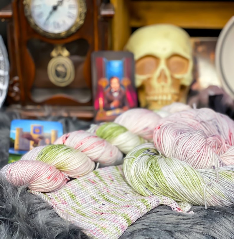 Pode incluir: Dois novelos de fio, um rosa e branco com manchas vermelhas, o outro verde e branco com manchas pretas. Tamb&eacute;m &eacute; mostrado uma pequena amostra de tric&ocirc; nas mesmas cores.