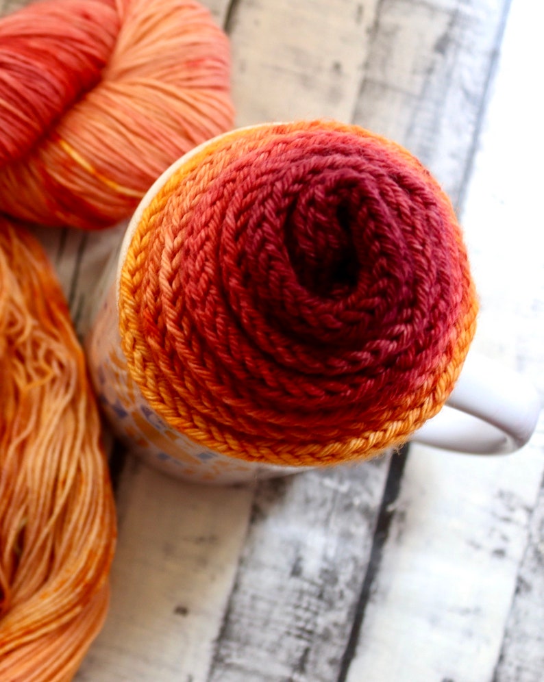 Peut inclure: Gros plan d'une tasse envelopp&eacute;e de fil orange, rouge et bordeaux. Le fil est enroul&eacute; en spirale, cr&eacute;ant un effet d&eacute;grad&eacute;.