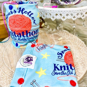 Könnte beinhalten: Zwei blaue und weiße Stoffbeutel mit roten Knöpfen. Ein Beutel hat den Text "Spars Hollow Knitathon The Old Muddy River Bridge" und eine rote Wollknäuel. Der andere Beutel hat den Text "PMIX Right Star Knit Save the Old" und einen gelben Stern.