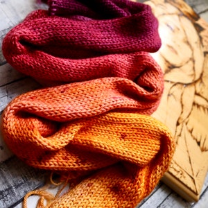 Peut inclure: Trois &eacute;charpes en tricot dans des tons d'orange, de rouge et de violet. Les &eacute;charpes sont empil&eacute;es les unes sur les autres, l'&eacute;charpe orange en bas, l'&eacute;charpe rouge au milieu et l'&eacute;charpe violette en haut.