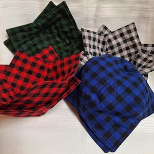 May include: Four fabric bowl cozies in different plaid patterns. The cozies are folded into a star shape. The colours are red, blue, black, and green.