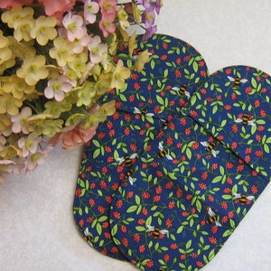 May include: Two navy blue oven mitts with a pattern of bees, red berries, and green leaves. The mitts are near a bouquet of colourful flowers.