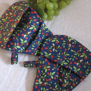 May include: Two navy blue oven mitts with a pattern of red strawberries, green leaves, and yellow and black bees. The mitts have a curved shape and a small loop for hanging.