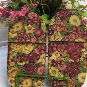 May include: A pair of floral print oven mitts with a dark background and a burgundy, yellow, and green floral pattern.