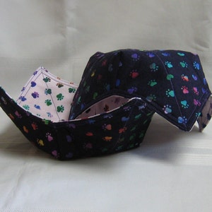 May include: Two fabric bowls with a paw print pattern. The bowls are folded and nested together. The outer bowl is dark blue with multi-coloured paw prints. The inner bowl is pink with multi-coloured paw prints.