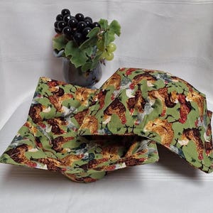 Peut inclure: Deux maniques carrées en tissu avec un motif de poulet sur fond vert. Les maniques sont pliées et empilées, mettant en valeur le motif de poulet. Un petit vase avec des raisins est en arrière-plan.