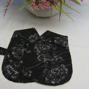 May include: A pair of black oven mitts with a white floral pattern. The mitts have a loop handle for easy gripping.