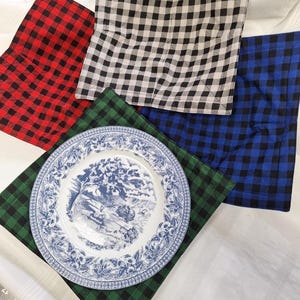May include: A blue and white patterned plate sits on a green and black checked placemat. Other placemats in red, black and white, and blue and black checked patterns are visible, suggesting a rustic or farmhouse style.
