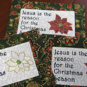 May include: Three white fabric squares with green and red floral patterns. Each square has a white embroidered patch with the text "Jesus is the reason for the Christmas Season" and a red or white poinsettia.