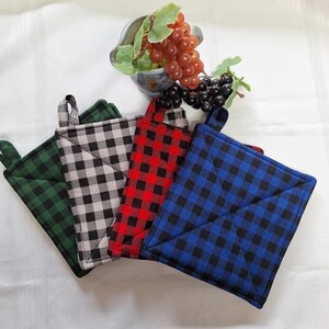 Peut inclure: Quatre maniques carrées à carreaux verts, gris, rouges et bleus. Chaque manique a une boucle pour être suspendue. Un petit bol de raisins est en arrière-plan.