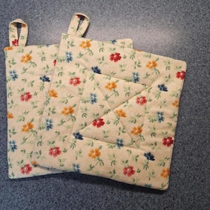 May include: Two beige quilted pot holders with a floral pattern in shades of red, orange, blue, and green.