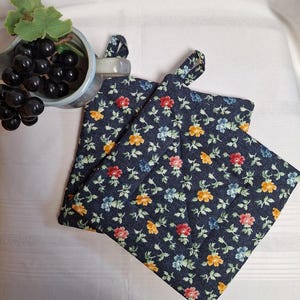May include: Two blue quilted pot holders with a floral pattern of small yellow, red, and blue flowers on a dark blue background.