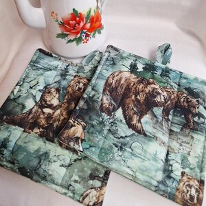 Peut inclure: Deux maniques de cuisine matelassées de couleur verte et marron avec un motif d'ours et d'ourson. Les maniques ont une texture matelassée et sont faites de tissu.