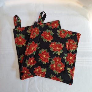 May include: Two black quilted pot holders with a red and gold poinsettia print.