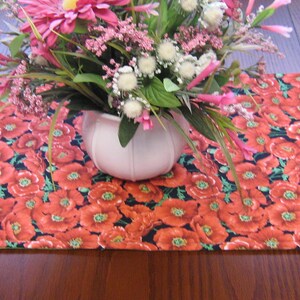 Peut inclure: Chemin de table floral avec un motif de coquelicots rouges et verts sur fond sombre. Un vase blanc contient un bouquet de fleurs roses et blanches, posé sur le chemin de table. Décoration d'intérieur.
