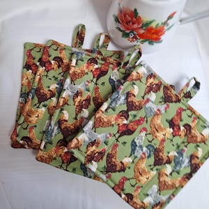 May include: Set of five green pot holders with a repeating pattern of colourful chickens. The pot holders have a loop handle on each side.