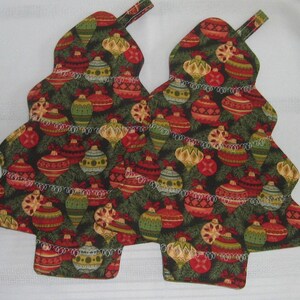 Peut inclure: Deux maniques de Noël en forme de sapin de Noël, vertes et rouges, avec une bordure blanche et un motif d'ornements.