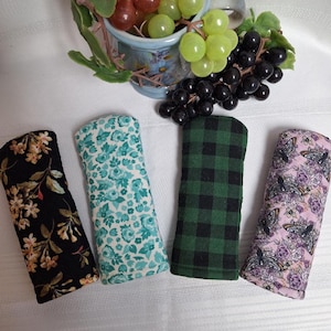 Peut inclure: Quatre étuis à lunettes en tissu avec différents motifs. L'un est noir avec un imprimé floral, un autre est turquoise avec un motif floral, un troisième est à carreaux verts et le dernier est rose avec des papillons et des fleurs. Un bol décoratif de raisins est en arrière-plan.
