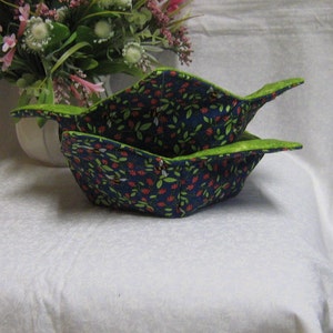 May include: Two blue and green fabric bowls with a floral pattern. The bowls are folded together and have a green trim.