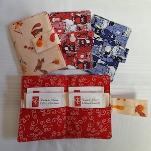 Peut inclure: Plusieurs portefeuilles et organisateurs en tissu. Les portefeuilles présentent divers motifs, notamment des écureuils, des chats et un motif tourbillonnant rouge. L'organisateur contient des sachets de thé. Fermetures à bouton.