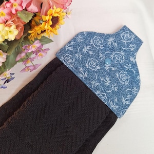 Peut inclure: Un torchon de cuisine noir avec un dessus en jean orné d'un motif floral blanc et d'un bouton bleu clair. Le torchon présente un motif tissé texturé. Un bouquet de fleurs colorées est en arrière-plan.