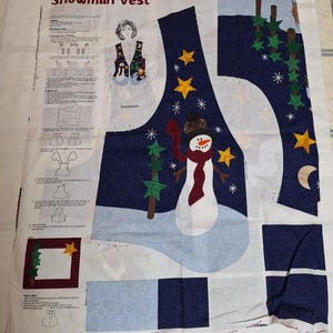 May include: A fabric panel for a Snowman Vest sewing project featuring printed instructions, a diagram of a person wearing the vest, and pre-printed pattern pieces on a dark blue background with snowmen, stars, and trees in white, red, and yellow.