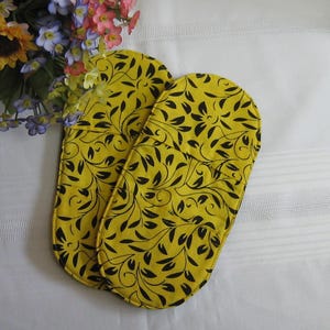 May include: Two yellow oven gloves with a black floral pattern. The gloves are made of fabric and have a quilted texture.