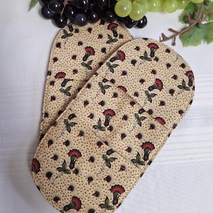 May include: A pair of beige oven gloves with a floral design of red flowers and green leaves. The gloves have a quilted pattern and are set against a white background. The floral pattern is repeated across the surface of the gloves.