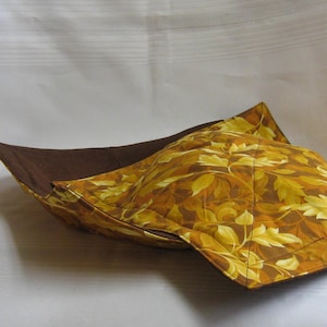 May include: A brown and gold fabric bowl with a leaf pattern. The bowl is folded and has a brown lining.