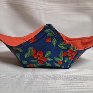Peut inclure: Un repose-bol en tissu avec un extérieur bleu orné d'un motif de cerises rouges et de feuilles vertes. L'intérieur du repose-bol est d'une couleur orange unie. L'objet présente quatre coins pointus et des coutures apparentes.