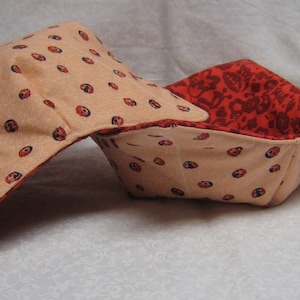 May include: Two fabric bowl cozies, one with a red floral pattern and the other with a pale pink background and black ladybug print.