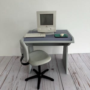 Puede incluir: Conjunto de escritorio de ordenador en miniatura con un monitor, teclado y ratón de estilo vintage. El escritorio y la silla son grises, lo que recuerda a una configuración de oficina retro. El escritorio mide unos 60 cm de ancho.