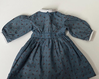 Könnte beinhalten: Ein blaues Kleid mit weißem Kragen und rotem Blumendruck. Das Kleid hat lange Ärmel und einen gerafften Rock.