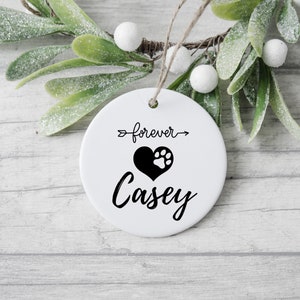 May include: White ceramic ornament with a black paw print inside a heart and the text "forever" with an arrow pointing to the right and the name "Casey" below the heart.