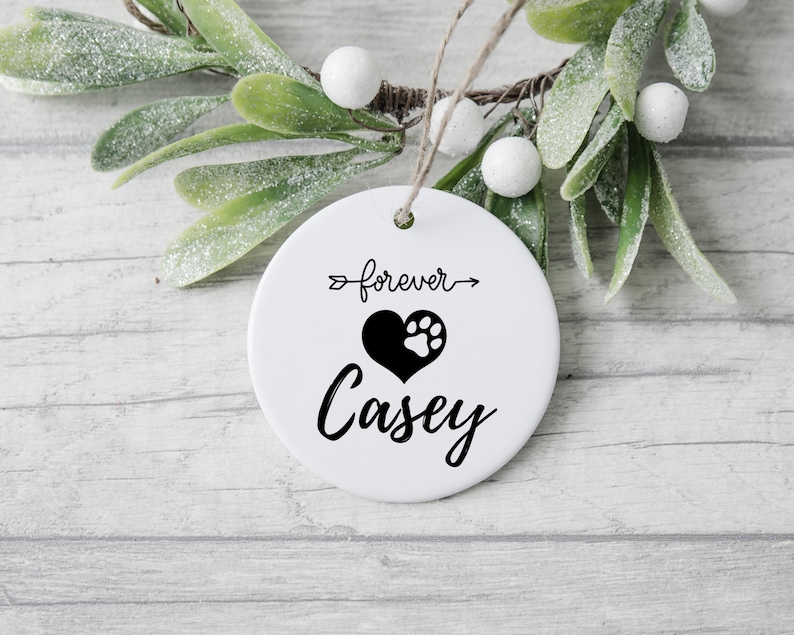 May include: White ceramic ornament with a black paw print inside a heart and the text "forever" with an arrow pointing to the right and the name "Casey" below the heart.