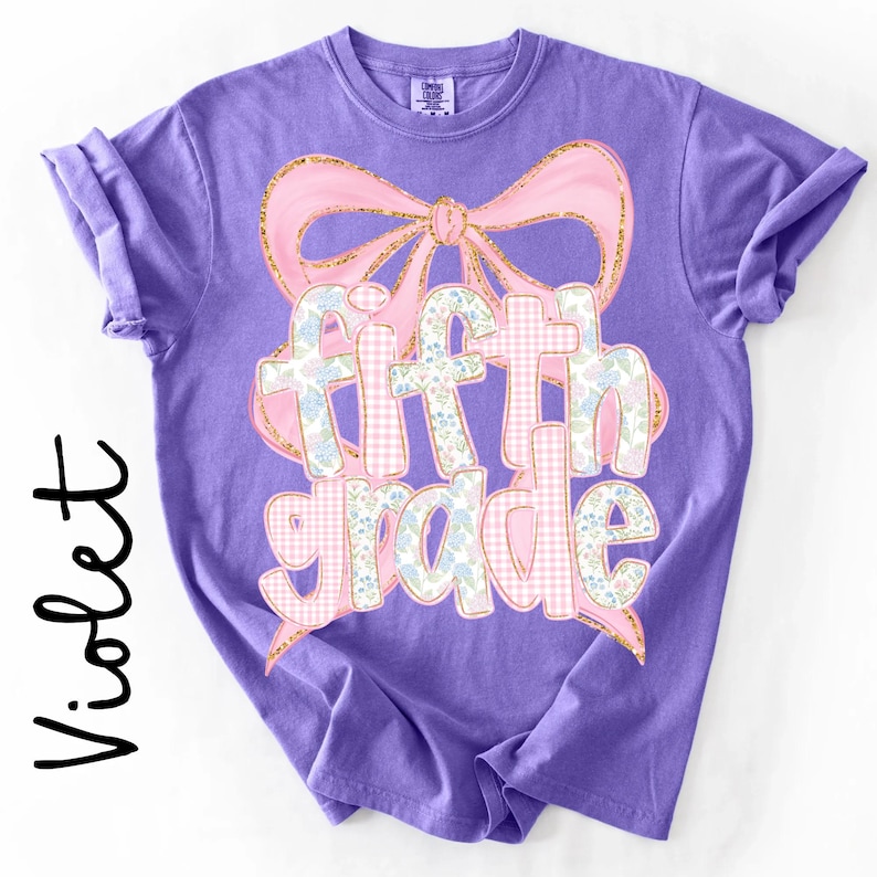 May include: A violet short-sleeve t-shirt featuring a large pink bow graphic with gold glitter outlines. The text fifth grade is printed in the center, with letters filled by a light pink gingham pattern and a blue and white floral print design.