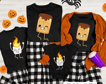 May include: Black t-shirts and a baby onesie with cartoon graphics of a marshmallow on fire and a s'more. The shirts are paired with black and white plaid pajama pants. The text "SHIRTS ONLY" is visible.