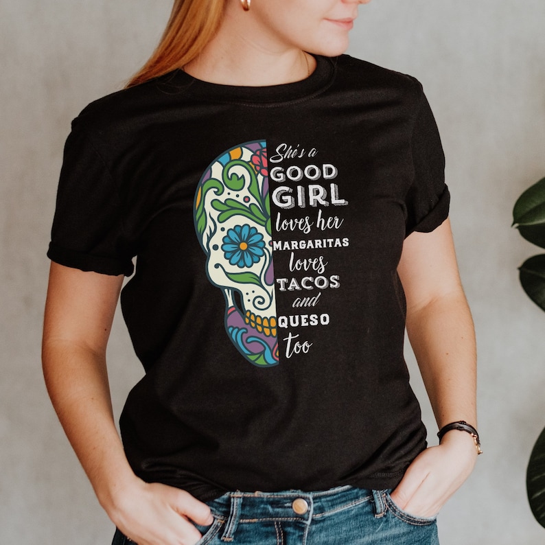 May include: Black t-shirt with a colorful sugar skull graphic and the text "She's a good girl loves her margaritas loves tacos and queso too".
