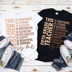 Puede incluir: Dos camisetas con el texto "This Grade Teacher is..." y una lista de atributos positivos. El texto est&aacute; en marr&oacute;n sobre una camiseta blanca y negra. Las camisetas est&aacute;n dispuestas sobre una superficie de madera con vaqueros y zapatillas.