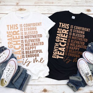 Puede incluir: Dos camisetas con el texto "This Grade Teacher is..." en ellas. El texto est&aacute; en diagonal e incluye las palabras "seguro", "fuerte", "bendecido", "motivado", "elevado", "melanizado", "feliz", "hermoso" y "suficiente". Una camiseta es blanca y la otra es negra.