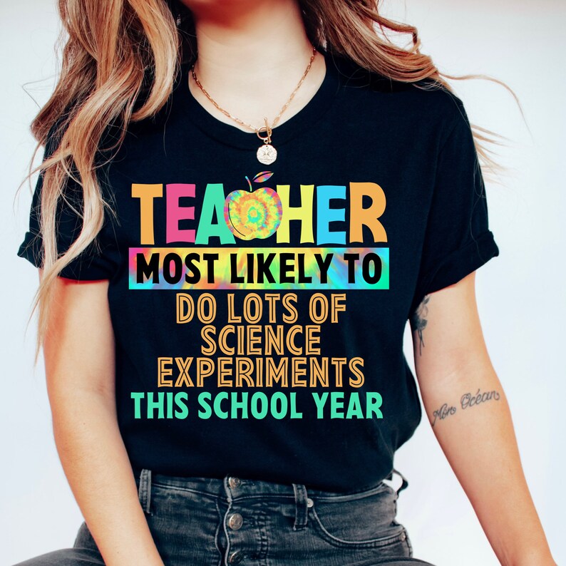 以下が含まれることがあります： タイダイ柄の黒いTシャツに「TEACHER MOST LIKELY TO DO LOTS OF SCIENCE EXPERIMENTS THIS SCHOOL YEAR」という文字が書かれています。